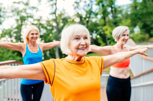 Group of beautiful sportive senior women training outdoors - Mature adults old friends doing fitness workout exercises in a park to stay healthy and fit - Foto, afbeelding