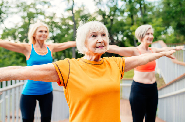 Group of beautiful sportive senior women training outdoors - Mature adults old friends doing fitness workout exercises in a park to stay healthy and fit - Fotografie, Obrázek