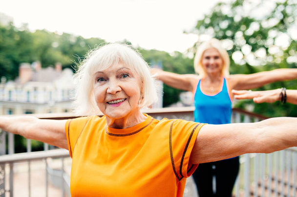 Group of beautiful sportive senior women training outdoors - Mature adults old friends doing fitness workout exercises in a park to stay healthy and fit - Foto, Imagem