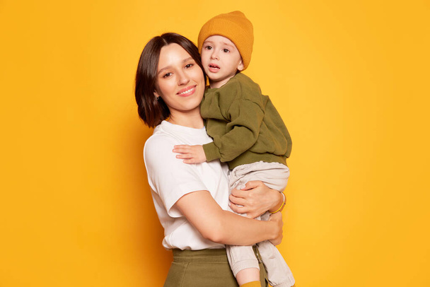 Hugs. Happy young mother with her cute little son posing isolated on bright yellow background. Emotions, family, love, motherhood and Mothers day concept. - Fotó, kép