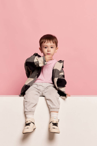 Portrait of cute little toddler boy sitting on big box and looking at camera. Emotions, kids fashion, happy childhood concept. Looks calm and sad. Copy space for ad - Фото, зображення