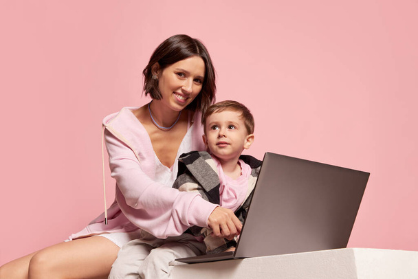 Cheerful young woman and little boy, mother and son using laptop isolated on pink studio background. Mothers Day celebration. Concept of family, childhood, motherhood, sincere emotions - Fotoğraf, Görsel