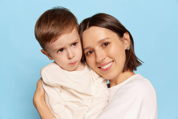 Tenderness. Half-length portrait of beautiful happy woman hugging her little son, kid isolated on blue background. Family, love, motherhood and Mothers day concept. - Photo, Image