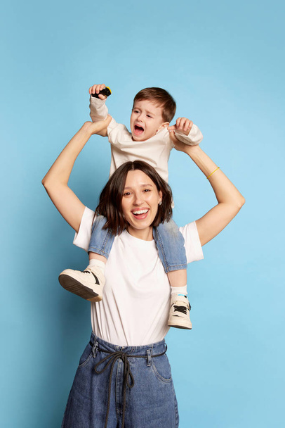 Little boy act up and cry. Mother with little kid isolated on blue background. Concept of emotions, Mothers Day, love, family and parenthood. Copy space for ad - Фото, зображення