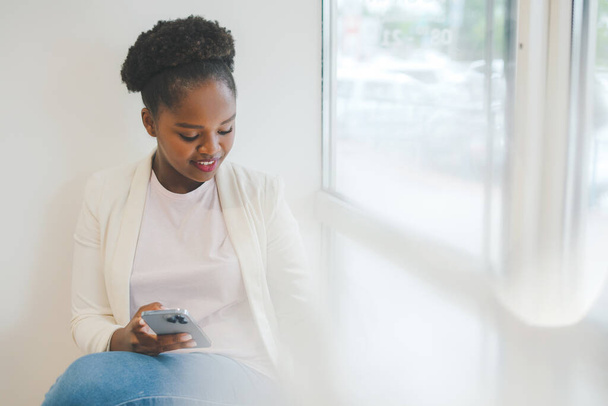 Afrikanerin schaut sich Video auf ihrem Handy an, während sie in einem Café sitzt und Kaffee trinkt. Attraktive schöne Mädchen. Positiver Mensch. Soziale Medien - Foto, Bild
