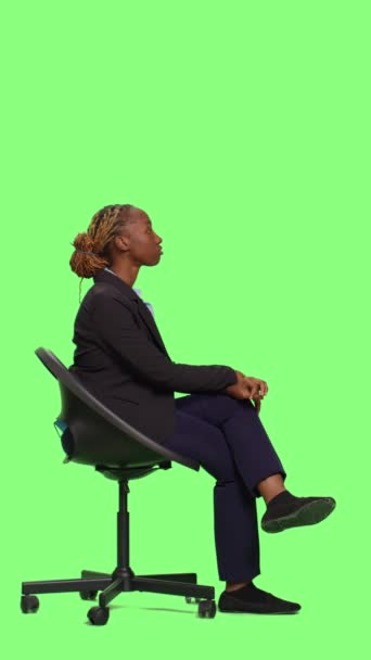 Vertikales Video: Unternehmensmanagerin sitzt auf Stuhl und wartet im Studio, Ganzkörper-Green-Screen-Hintergrund. Junge Geschäftsfrau im Anzug wartet und sitzt, um sich in Erwartung vorzubereiten, Greenscreen - Filmmaterial, Video