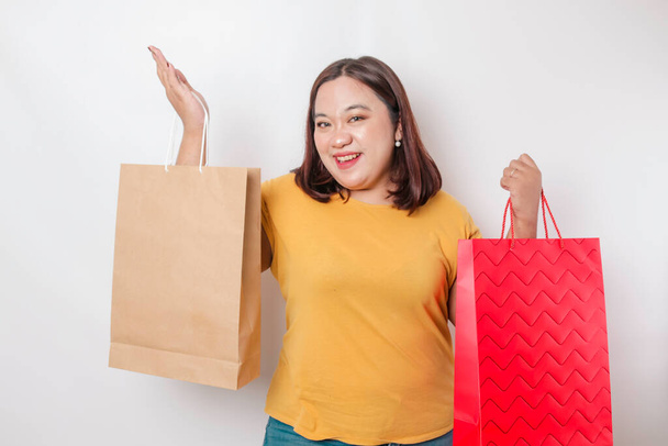 Mutlu, genç, Asyalı, iri yarı bir kadın sarı gömlek giyiyor ve elinde hediye kutusu ve alışveriş çantası tutuyor.. - Fotoğraf, Görsel