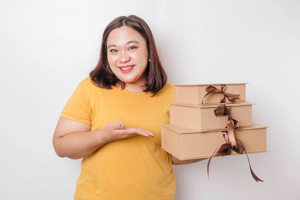 A happy young Asian big sized woman is wearing yellow shirt and holding presents box and shopping bag. - Foto, immagini