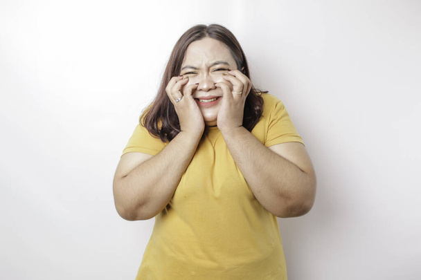 A portrait of an Asian big sized woman wearing a yellow t-shirt isolated by white background looks depressed - Фото, изображение