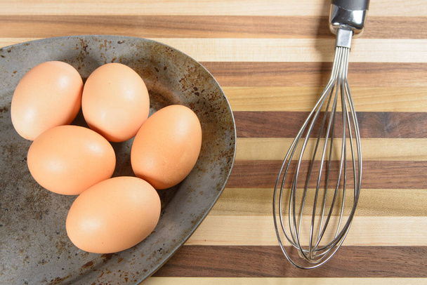 Uma placa de metal rústico com seis ovos castanhos com um wisk e tábua de corte. - Foto, Imagem