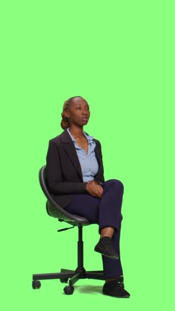 Vertikales Video: Büroangestellte sitzt auf einem Stuhl und wartet im Studio, Ganzkörper-Hintergrund mit grünem Bildschirm. Junge Geschäftsfrau im Anzug wartet und sitzt, um sich in Erwartung vorzubereiten, Greenscreen-Hintergrund. - Filmmaterial, Video