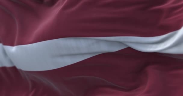Vista de cerca de la bandera nacional de Letonia ondeando. La República de Letonia es un estado situado en el noreste de Europa. Fondo texturizado de tela. Enfoque selectivo. Lazo inconsútil en cámara lenta - Metraje, vídeo