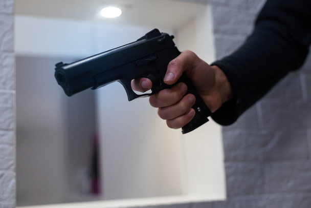Lőfegyverekkel való fenyegetés. A pisztoly csöve férfi kézben a kamerára mutat. A férfi bűnözőknél fekete háttér van. Támadás vagy védelem. - Fotó, kép