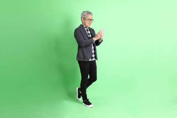 de 40s volwassen aziatische man stnading op de groene achtergrond met slimme casual kleding. - Foto, afbeelding