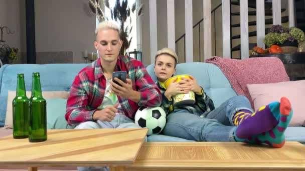 幸運な男は屋内でカメラにスマートフォンの緑のクロマキー画面を示して、利益スポーツベットを持っています。テレビで生放送のスポーツ試合を見ているサッカーファンは、自宅で好きなサッカーチームを応援 - 映像、動画