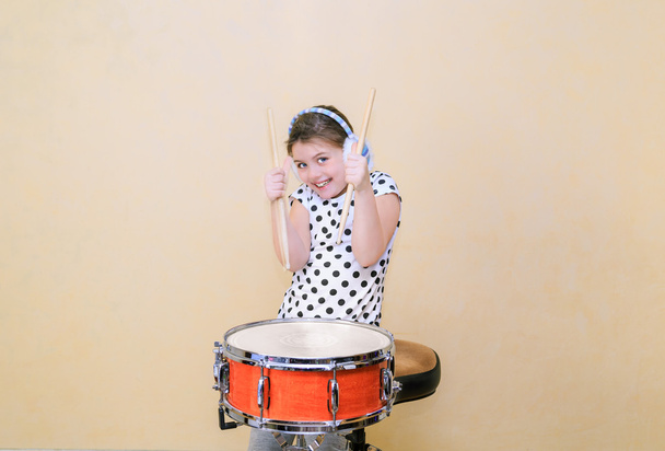 Joyful, charming fashionable little girl  in motion sitting behind the snare drum and holding a sticks in her hands - Photo, Image
