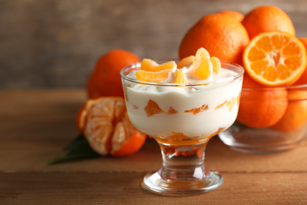 Tasty milk dessert with fresh tangerine pieces in glass bowl, on wooden background - Foto, Imagem