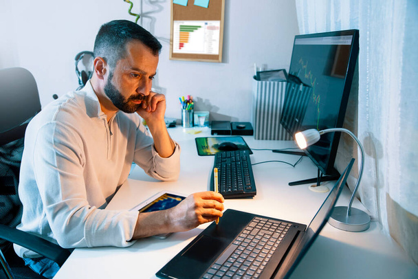 Занятый взрослый человек, работающий за своим столом, используя компьютер, ноутбук и цифровой планшет. Мультимедиа программист - Фото, изображение