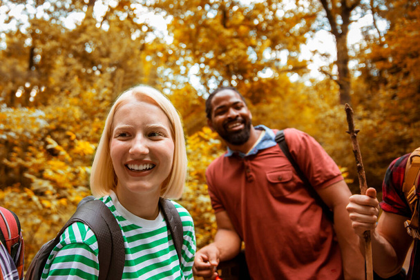 Smiling happy Multiracial couple walking in woods. Backpacker Friends on tracking in beautiful autumn forest - 写真・画像