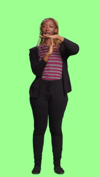 Vertical video: Full body of woman doing t shape timeout symbol on green screen backdrop, showing break or pause gesture with arms. Standing on greenscreen background with negative refusal symbol. - Footage, Video