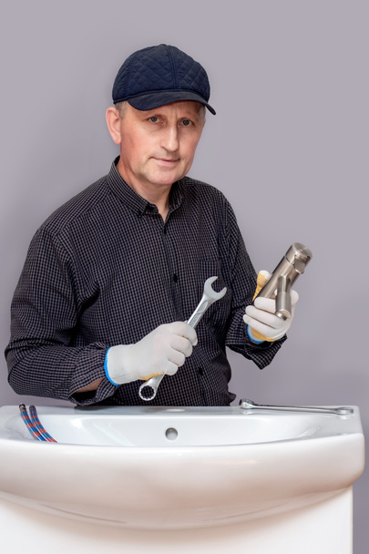 Мастер сантехник с гаечным ключом в руке прикручивает кран к раковине в ванной. - Фото, изображение