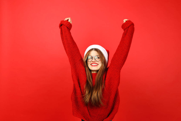 New Year party. Beautiful woman in santa hat with raised hands on red christmas background. - Photo, Image