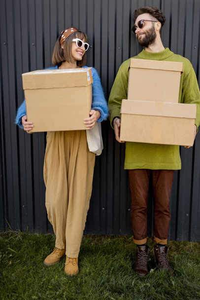 Portrait of young and stylish couple standing with cardboard parcels together outdoors. Concept of delivery and e-shopping - Photo, Image