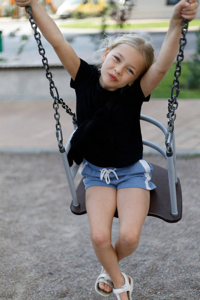 Portrait of a cute child on a swing at the playground. - Фото, зображення