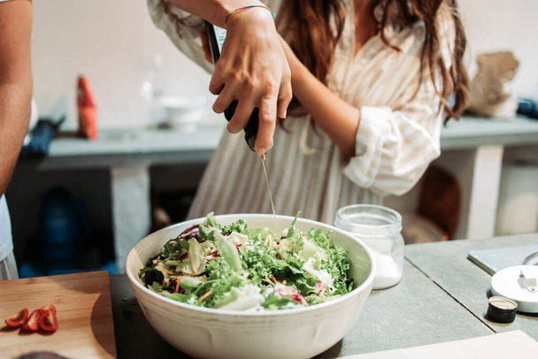 Mano femminile versando olio d'oliva sull'insalata di verdure fresca - Foto, immagini