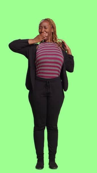 Függőleges videó: Az afro-amerikai személy teljes teste ásít és fáradt, zöld háttér felett áll. Felnőtt viselkedés kimerült és érdektelen, elalvás és fáradtság érzése - Felvétel, videó