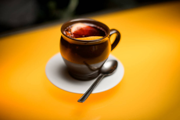 Close-up of cup of tea with lemon on white saucer with spoon on yellow table - Foto, imagen