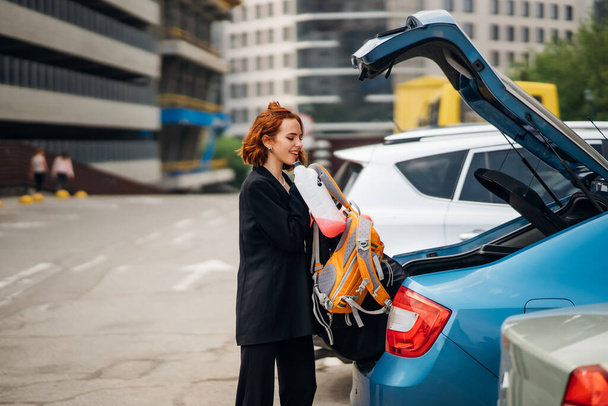 Μια νεαρή γυναίκα πακετάρει αποσκευές στο πορτ-μπαγκάζ του αυτοκινήτου. - Φωτογραφία, εικόνα