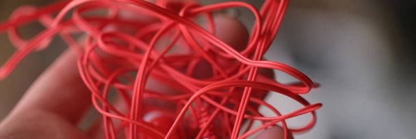Tangled red headphones in hand. Person trying to unravel broken headphones concept - Fotografie, Obrázek