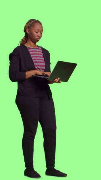 Вертикальне відео: Сучасна молода жінка тримає ноутбук і переглядає Інтернет, використовуючи портативний ПК для прокрутки через веб-сайт. усміхнена щаслива дівчина стоїть на повному тлі зеленого екрану, соціальна
 - Кадри, відео