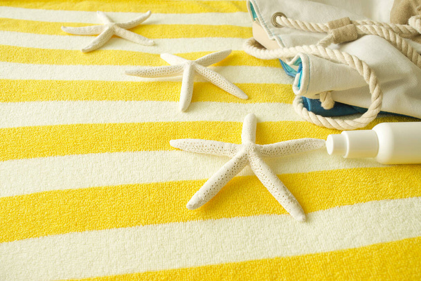 The concept of travel, vacation, summer, beach items, resort hotel. On a striped yellow towel lies a canvas bag, sunscreen and starfish. Copy space. Nobody. - Foto, imagen