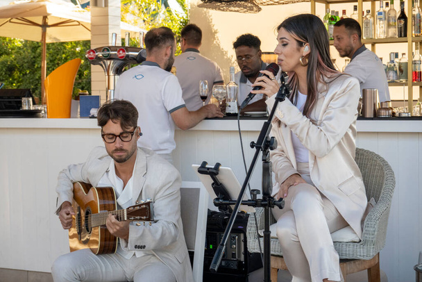 QUINTA DO LAGO, PORTUGAL - 26th JUNE 2022: Band duo singer and guitar player called Beatriz playing in a beach bar restaurant in Quinta do Lago. - Photo, image