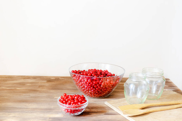 Red currants in bowl preparing for making jam in jars at home kitchen for winter.peeling summer fruits, cooking, recipe instruction. Natural,healthy frozen berry rich in vitamins on wooden table. - Fotografie, Obrázek