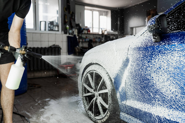 Druhá fáze podrobného mytí v autoservisu. Myčka aut myje celé tělo. Proces postřiku pěny na karoserii auta v garáži - Fotografie, Obrázek