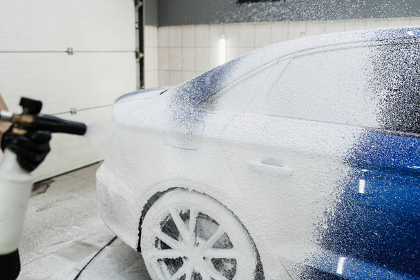 Proceso de pulverización de espuma en la carrocería del coche en el garaje. Segunda fase de detalle del lavado en el servicio de automóviles. Lavadora de coches hace lavado de coches de cuerpo completo - Foto, imagen