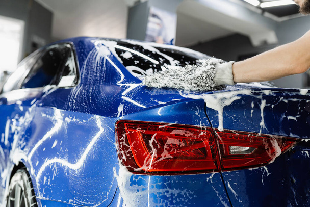 ガレージに泡車のボディとマイクロファイバー手袋で手を洗う。自動車詳細サービスで手動フォーム洗浄を行う車の洗濯機 - 写真・画像