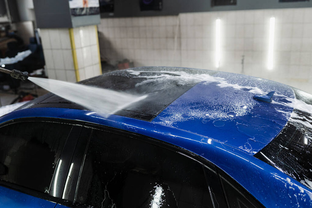 Rozpylanie wody na samochód, aby zmyć pianę w garażu. Proces szczegółowego mycia w serwisie samochodowym. Myjka samochodowa do mycia całego ciała - Zdjęcie, obraz