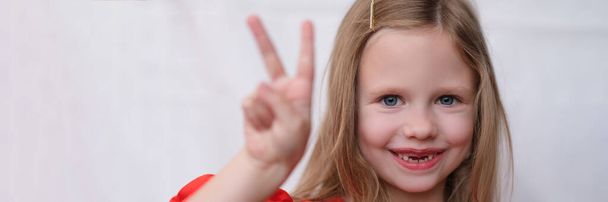 Mosolygó kislány első fogak nélkül két ujjal felfelé. A pozitív gyerekes hangulat koncepciójának portréja - Fotó, kép