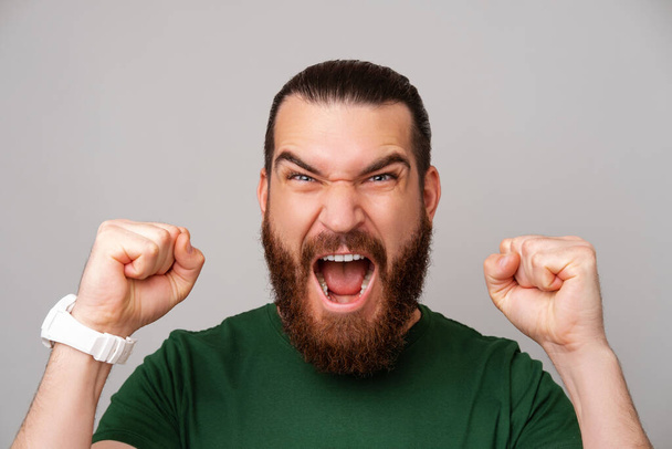 Close up photo of amazed bearded man screaming and celebrating victory over grey backdrop. - Foto, Imagen