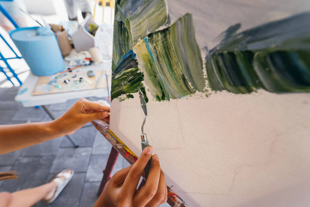 Primer plano de una mano de mujer aplicando pintura a un lienzo con una espátula - Foto, Imagen