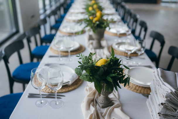 Mesa festiva en la fiesta de bodas están decoradas con arreglos de limón, en la mesa hay platos con servilletas y vasos - Foto, Imagen
