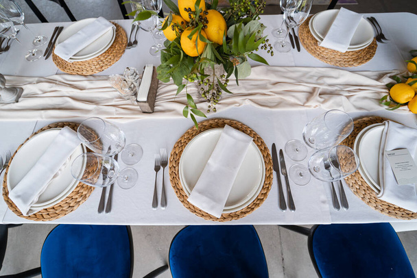 Святковий стіл на весіллі прикрашені лимонними аранжуваннями, на столі стоять тарілки з серветками і келихами
 - Фото, зображення
