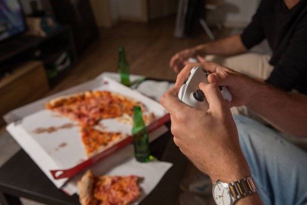 Вечер друзей, наслаждающихся консольными играми во время еды пиццы и питья пива. - Фото, изображение