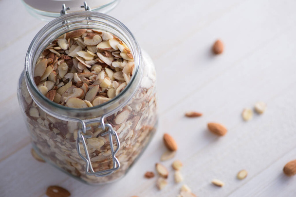 Raw sliced almonds in a clasping glass jar on white table. - Valokuva, kuva