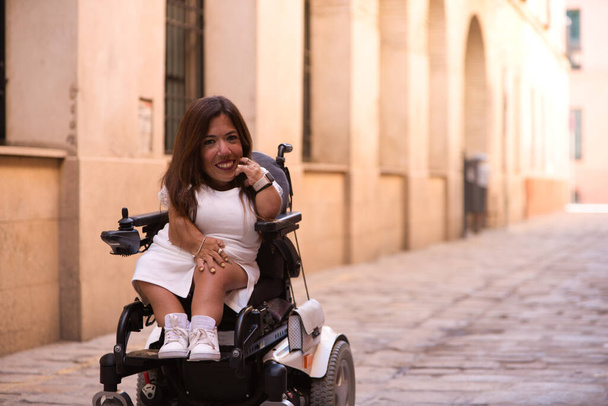 beautiful young disabled woman in wheelchair and reduced mobility enjoys her trip around the city where she is on vacation. - Photo, Image