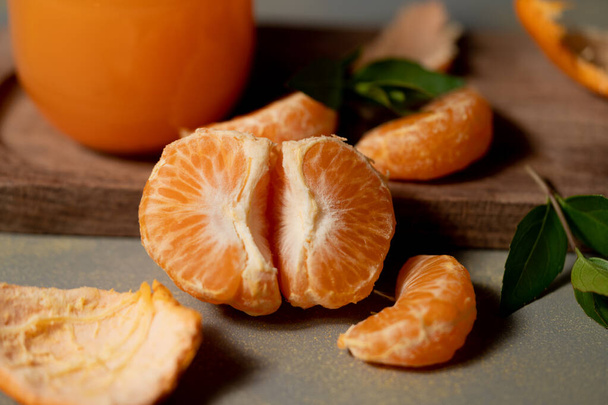 close-up van enkele mandarijnsegmenten. van achteren zie je een glas met sap van deze sinaasappelcitrusvruchten. alles staat op een houten plank. - Foto, afbeelding
